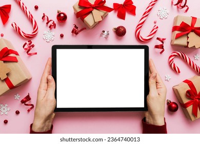 Christmas online shopping from home, female hands holding tablet pc with blank white display top view. woman hand holding tablet with blank screen, Christmas tree and gifts on background. - Shutterstock ID 2364740013