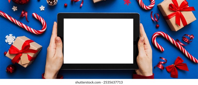 Christmas online shopping from home, female hands holding tablet pc with blank white display top view. woman hand holding tablet with blank screen, Christmas tree and gifts on background. - Powered by Shutterstock