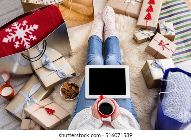 Christmas online shopping top view. Female buyer touch black screen of tablet, copy space. Woman has coffee, buys presents, prepare to xmas eve, sit near gifts boxes and packages. Winter holiday sales