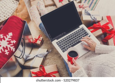 Christmas online shopping top view. Female buyer with laptop, copy space on screen. Woman has coffee, buys presents, prepare to xmas eve, sitting among gifts boxes and packages. Winter holidays sales