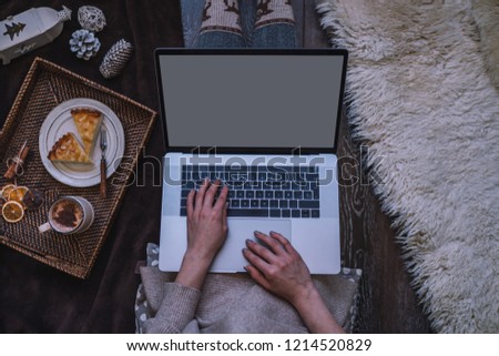 Christmas online shopping. Woman buys presents, prepare to xmas eve. Female with laptop, copy space on screen. Hot coffee, spice and almond cakes on tray. Cozy blanket. Toned image. Soft focus.