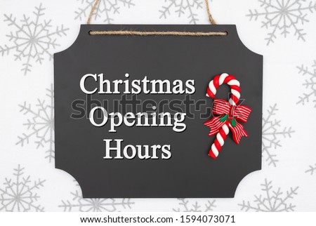 Christmas opening hours message on hanging chalkboard with a candy cane and white and gray snowflakes
