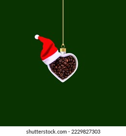 Christmas ornament made of white heart shaped bowl with coffee beans and Santa hat on dark green table background. Flat lay, top view, copy space. New Year sale card. Coffee lovers. - Powered by Shutterstock