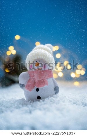 Christmas ornament snowman in the snow and bokeh lights. Abstract winter, seasonal background