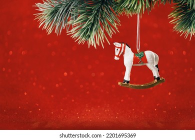 Christmas Ornaments. Rocking Horse Toy Pendant On Christmas Tree Branch. Happy New Year Greeting Card. Copy Space Banner. Red Background With Bokeh Lights.