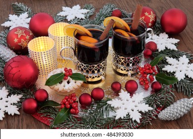 Christmas Party Food And Drink With Mulled Wine And Mince Pie, Bauble Decorations, Holly And Snow Covered Fir.