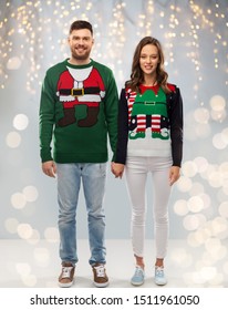 Christmas, People And Holidays Concept - Happy Couple At Ugly Sweater Party Over Festive Lights Background