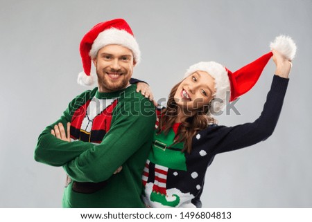 christmas, people and holidays concept - portrait of happy couple in santa hats at ugly sweater party