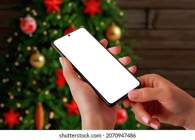 Christmas Phone Mockup Concept. Smart Phone In Woman Hands Front Off Christmas Tree. Isolated Display For App Promotion