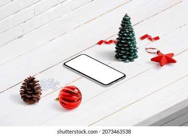 Christmas Phone Mockup In Isometric Position. Composition On White Wooden Desk. Isolated Phone Display For App Design Promotion