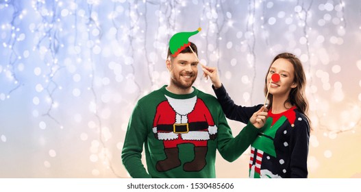 Christmas, Photo Booth And Holidays Concept - Happy Couple In Ugly Sweaters Posing With Party Props Over Festive Lights Background