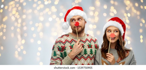 Christmas, Photo Booth And Holidays Concept - Happy Couple In Ugly Sweaters Posing With Party Props Over Festive Lights Background