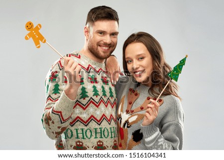christmas, photo booth and holidays concept - happy couple in ugly sweaters posing with party props