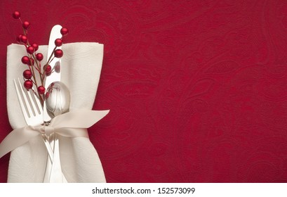 Christmas Place Setting With Sterling Silverware In White Napkin And Ribbon On Red Background With Copy Space Or Room For Your Text Or Words.