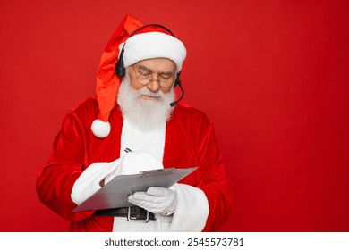 Christmas portrait of Santa Claus wearing headset holding clipboard writing a list children presents isolated over a red background, copy space. Call center concept - Powered by Shutterstock