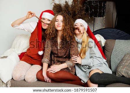 Christmas portrait of three attractive funny women sisters with red santa hat and curly hair