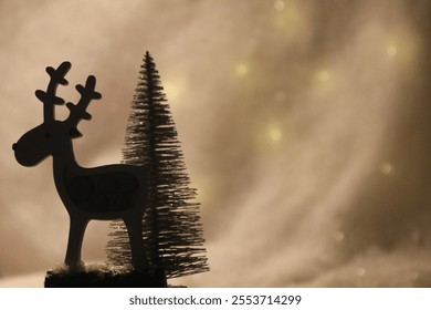 Christmas postcard with a reindeer and a tree, with snow in the background and warm light. Defocused golden background lights. Reindeer with dark silhouette - Powered by Shutterstock