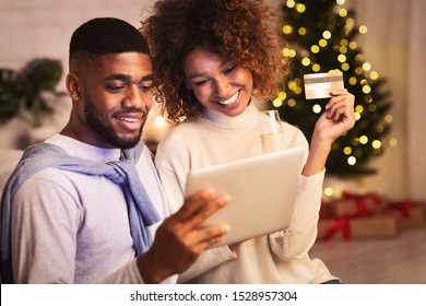 Christmas Preparation. Happy Black Couple Buying Gifts Online, Using Tablet And Credit Card