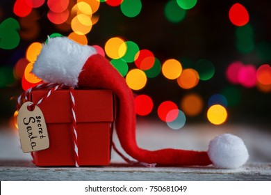 Christmas Present Or Box For Secret Santa With Santa Hat On Colorful Bokeh Background.