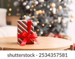 Christmas present on table against blurred Christmas tree in living room, closeup