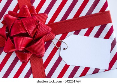 Christmas present wrapped in red and white striped wrapping paper red ribbon and bow and blank tag sitting on white background