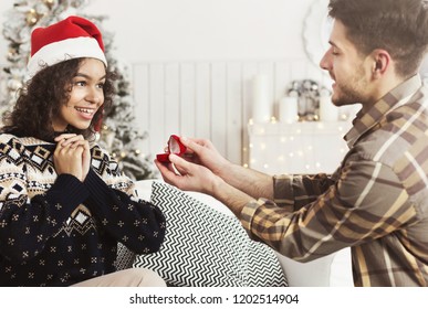 Christmas Proposal. Handsome Man Giving Engagement Ring To Excited Black Woman, Copy Space