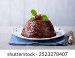 Christmas pudding, fruit cake on white plate. Traditional festive dessert. Close up. Grey background.