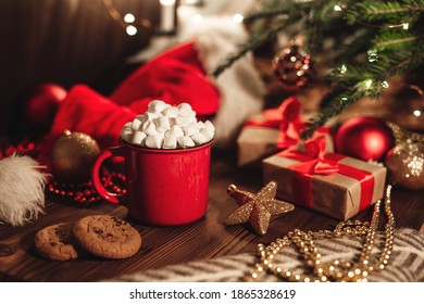 Christmas red mug with cocoa and marshmallows and cookies on a wooden table. New Year's home still life with a Christmas tree, a Santa hat and festive decorations. - Powered by Shutterstock