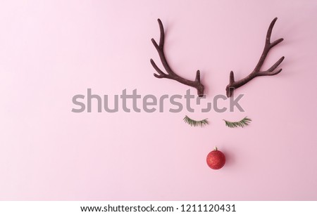 Christmas reindeer concept made of evergreen fir, red bauble decoration and antlers on pastel pink background. Minimal winter holidays idea. Flat lay top view composition.