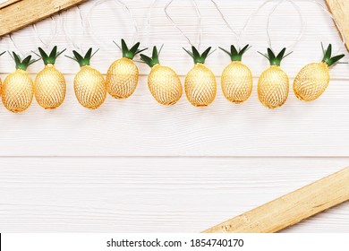 Christmas rustic background with string lights as pineapples golden colored on white wooden. Festive decoration, New Year fairy garland. Flat lay. Top view, copy space.