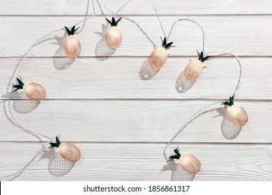 Christmas rustic background with string lights as pineapples golden colored on white wooden. Festive decoration, New Year fairy garland. Flat lay. Top view, copy space.