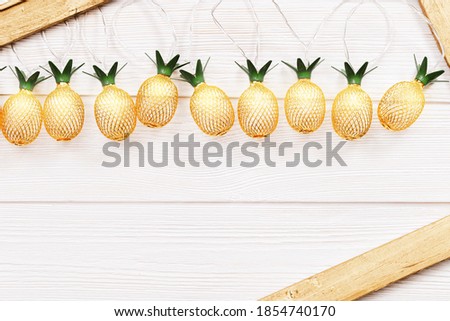 Christmas rustic background with string lights as pineapples golden colored on white wooden. Festive decoration, New Year fairy garland. Flat lay. Top view, copy space.
