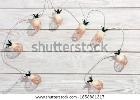 Christmas rustic background with string lights as pineapples golden colored on white wooden. Festive decoration, New Year fairy garland. Flat lay. Top view, copy space.
