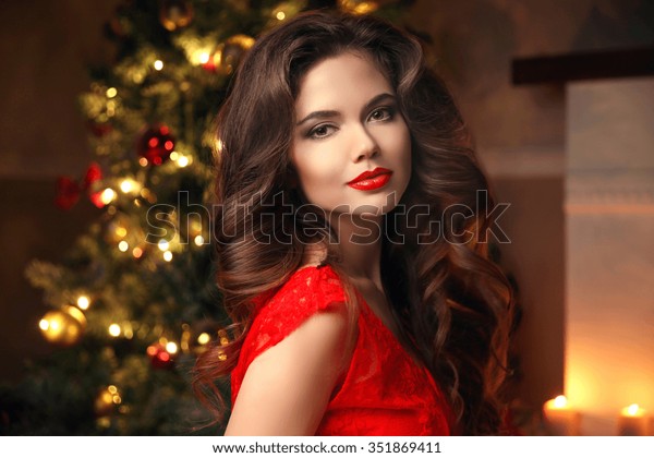 クリスマスサンタ 美しい笑顔の女性モデル メイクアップ ヘルシーな長髪 クリスマスツリーの光の背景に赤いドレスを着た優雅な女性 新年おめでとう の写真素材 今すぐ編集
