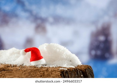 Christmas Santa Claus hat decoration on wooden board with copy space for products. Blurred background of snowy forest and trees in snowy winter. Snow falling - Powered by Shutterstock