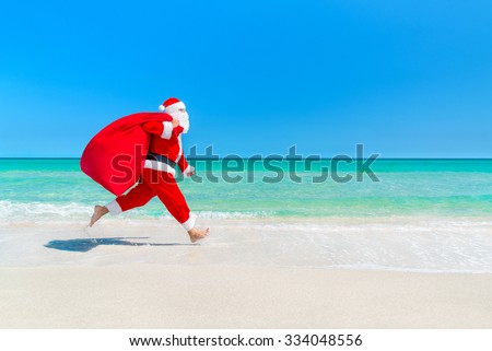 Christmas Santa Claus running with big sack full of gifts hurry on present for children along ocean tropical sandy beach - xmas travel vacation discounts and travel agencies price reductions concept