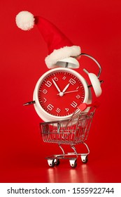 Christmas Santa Hat On Red Clock, Balanced In Shopping Cart. Last Minute Christmas Shopping Concept.