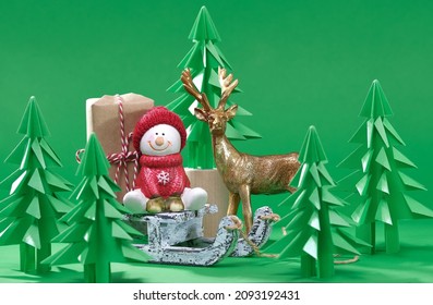 Christmas Scene. Christmas Snowman With Gift On Wooden Sled. Green Origami Fir Tree On A Green Background. Christmas Tree Paper Cutting Design Card. New Year Background With Paper Fir Tree