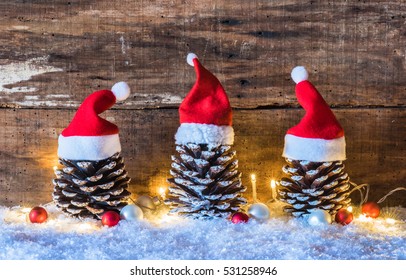 Christmas season, rustic decoration, Santa hats on pine cones with lights at snow and brown wooden background. - Powered by Shutterstock