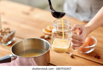 Christmas And Seasonal Drinks Concept - Close Up Of Hands With Ladle Pouring Eggnog From Pot To Glass Mug At Home