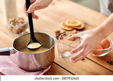 Christmas And Seasonal Drinks Concept - Close Up Of Hands With Ladle Pouring Eggnog From Pot To Glass At Home