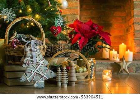 Christmas setting background: decorated Christmas tree, decorations pine cones in the basket, poinsettia with fireplace on the background; candles and lights, selective focus. Toned photo