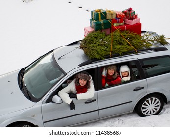 Christmas Shopping, Celebrating - The Family Is Riding A Car With Christmas Tree And Gifts On The Roof Of The Car