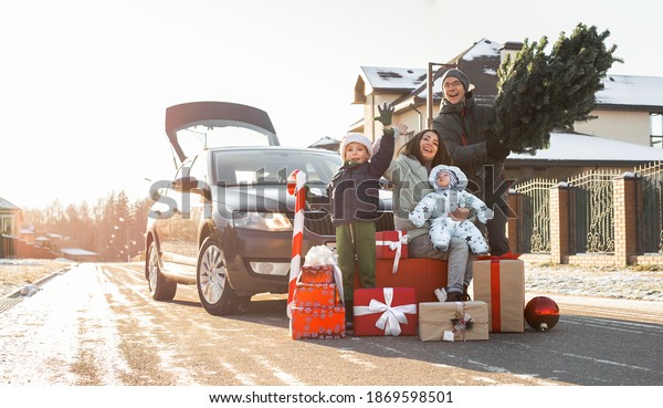 Christmas\
shopping and family preparation for winter holidays. Happy parents\
and cheerful children with many gifts and Xmas fir tree outside\
near car in town or country. Family of\
four