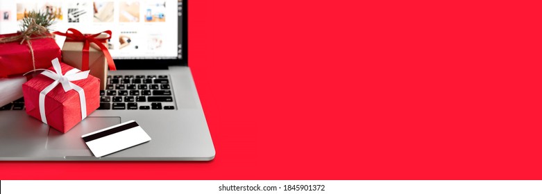 Christmas shopping online concept. Laptop with red gifts and credit card on the red background. Banner, copy space, mock up. Holiday winter sales, discounts, e-commerce