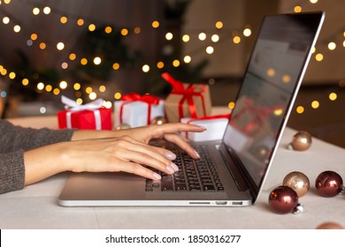 Christmas Shopping Online, Sales And Discounts Promotions During Winter Holidays, Online Shopping At Home And Lockdown Coronavirus. Female Hands On The Laptop With Gifts And Blurred Bokeh Lights