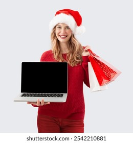 Christmas shopping online, smiling woman in santa hat showing laptop computer blank screen while holding a gift bags, Adv for top offers in Christmas presents web store or booking holiday xmas travel - Powered by Shutterstock