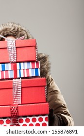 Christmas Shopping Stress - A Woman In A Winter Anorak Is Hidden Behind A Tall Stack Of Colorful Decorative Christmas Presents As She Returns From A Day Out Purchasing Gifts