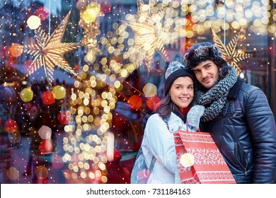 Christmas Shopping Together. Young Happy Couple Doing Christmas Shopping. Christmas Lights In The Background.