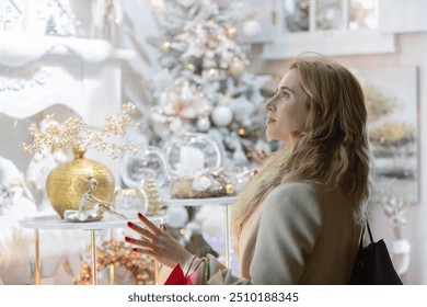 Christmas shopping woman, looks amazed and happy at the shop windows decorated with lights and figures. The young woman in front of a shop window thinking about what to buy for her Christmas gifts. - Powered by Shutterstock